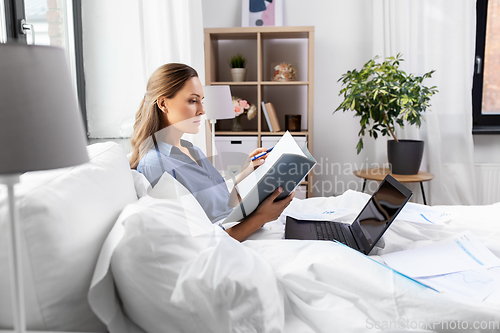 Image of young woman with laptop and papers in bed at home