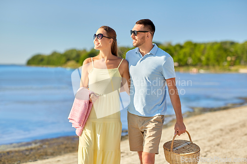 Image of happy couple with picnic basket walking on beach