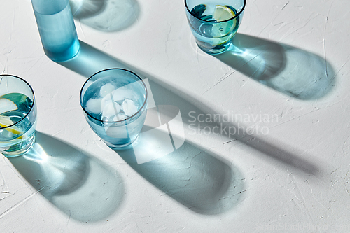 Image of glasses with water and lemons on white background