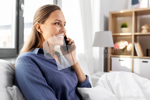 Image of happy woman calling on smartphone in bed at home