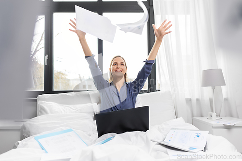 Image of happy woman with laptop and papers in bed at home