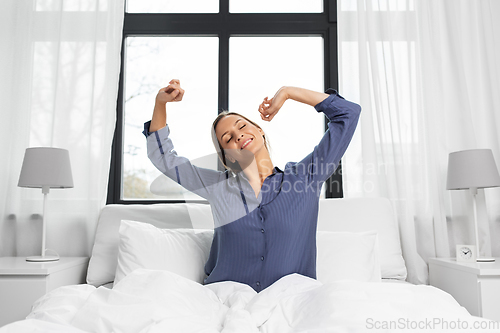 Image of happy woman stretching in bed at home