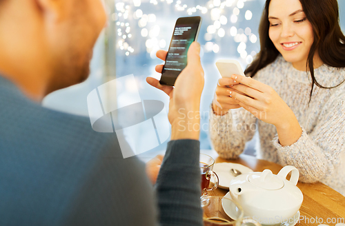 Image of happy couple with smartphones drinking tea at cafe