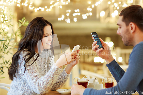 Image of happy couple with smartphones drinking tea at cafe