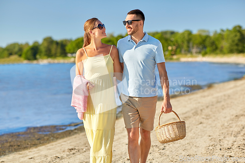 Image of happy couple with picnic basket walking on beach