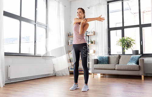Image of smiling young woman stretching arm at home
