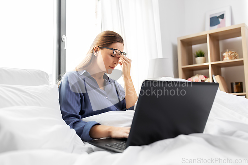 Image of tired woman in glasses with laptop in bed at home