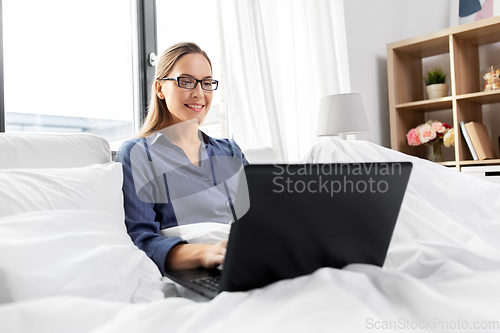 Image of young woman with laptop in bed at home bedroom