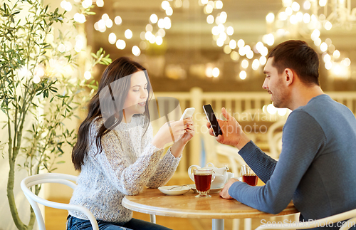 Image of happy couple with smartphones drinking tea at cafe