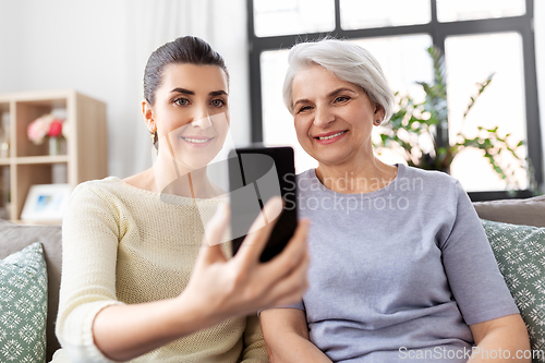 Image of senior mother with daughter taking selfie at home