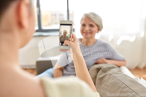 Image of adult daughter photographing senior mother at home