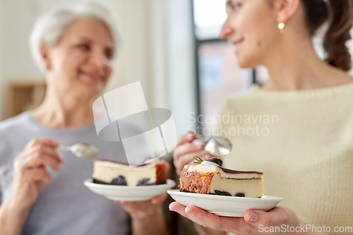 Image of old mother and adult daughter eating cake at home