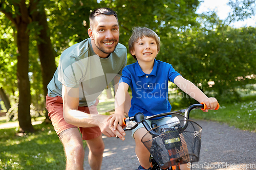 Image of father teaching little son to ride bicycle at park