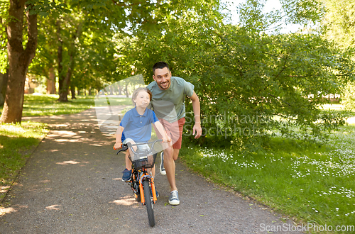 Image of father teaching little son to ride bicycle at park