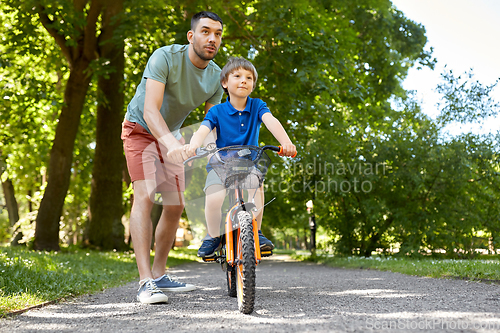 Image of father teaching little son to ride bicycle at park