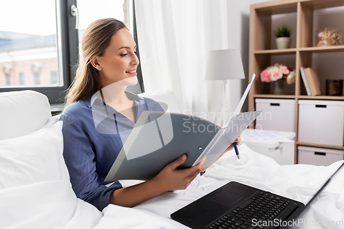 Image of happy woman with laptop and folder in bed at home