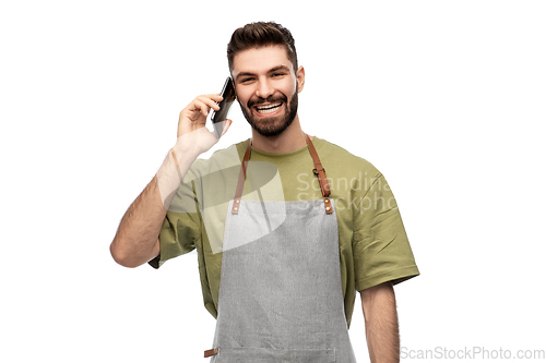 Image of happy barman in apron calling on smartphone