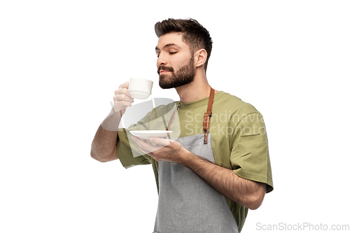 Image of happy barista or waiter in apron drinking coffee