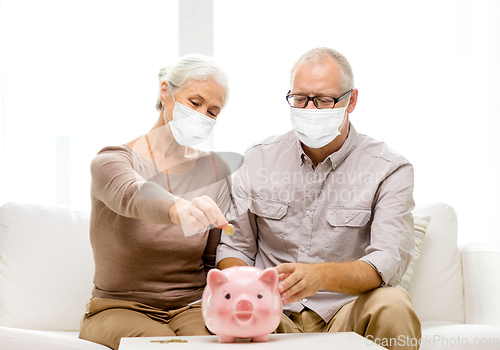 Image of old couple in masks putting coin into piggy bank