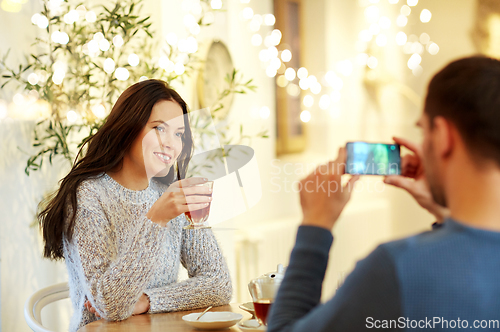 Image of man taking picture of woman by smartphone at cafe