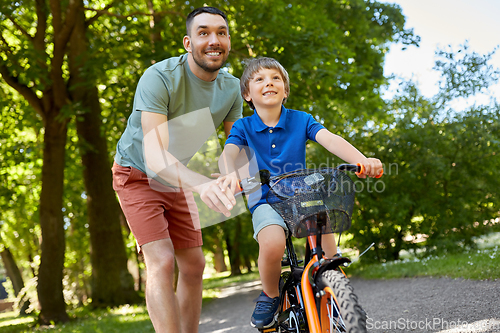 Image of father teaching little son to ride bicycle at park