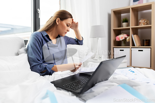 Image of young woman with laptop and papers in bed at home