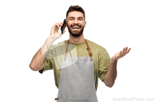 Image of happy barman in apron calling on smartphone