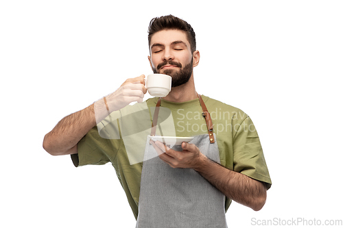 Image of happy barista or waiter in apron drinking coffee
