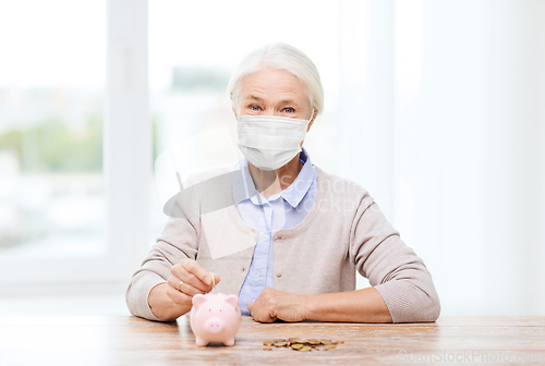 Image of old woman in mask putting coin into piggy bank