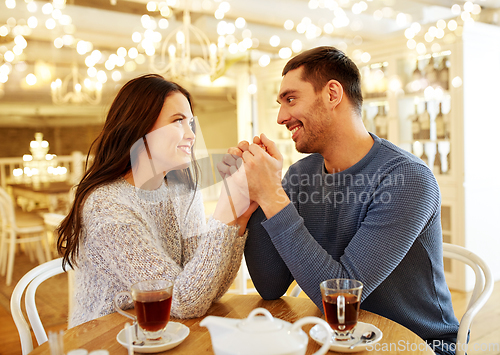 Image of happy couple with tea holding hands at restaurant