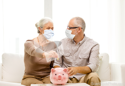 Image of old couple in masks putting coin into piggy bank