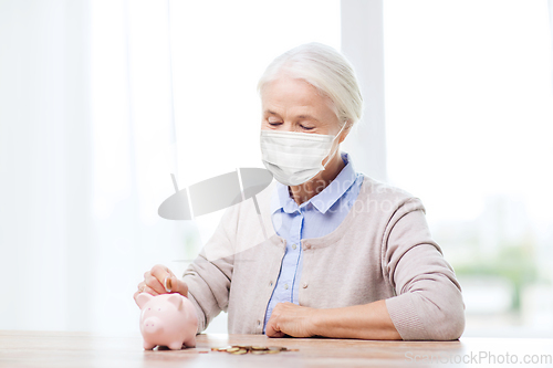 Image of old woman in mask putting coin into piggy bank