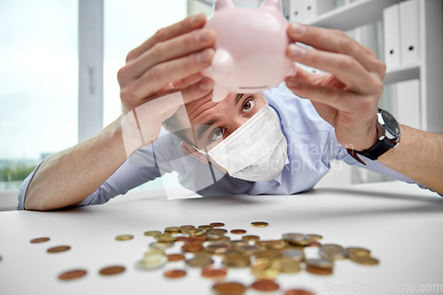 Image of businessman in mask shaking piggy bank for money