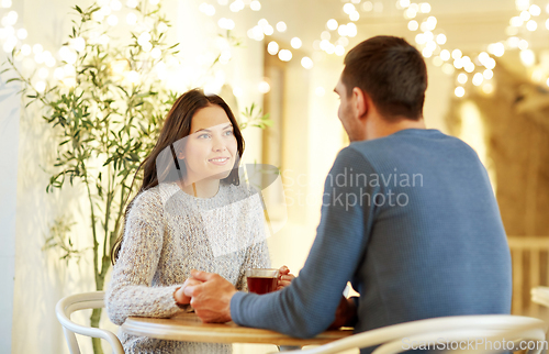 Image of happy couple with tea holding hands at restaurant