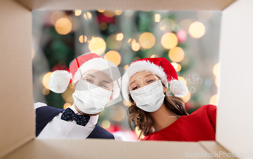 Image of couple in medical masks opening christmas gift box
