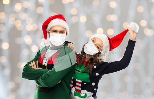 Image of couple in masks, christmas sweaters and santa hats