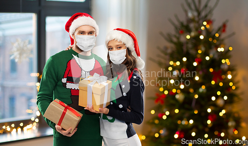 Image of couple in masks, christmas sweaters with gifts