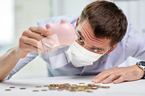 Image of businessman in mask shaking piggy bank for money