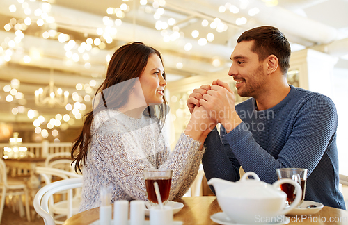 Image of happy couple with tea holding hands at restaurant