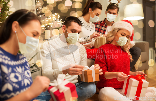 Image of friends in masks opening christmas gifts at home