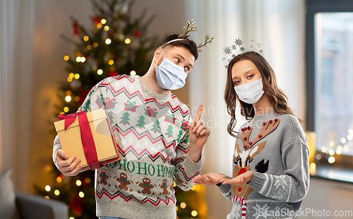 Image of couple in masks, christmas sweaters with gifts