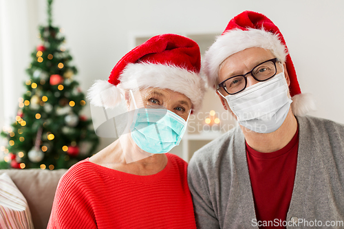 Image of senior couple in masks and santa hats on christmas