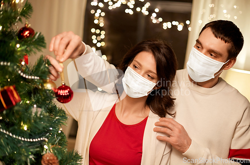 Image of couple in masks decorating christmas tree at home