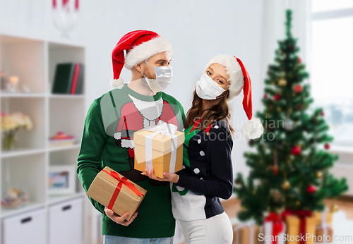 Image of couple in masks, christmas sweaters with gifts