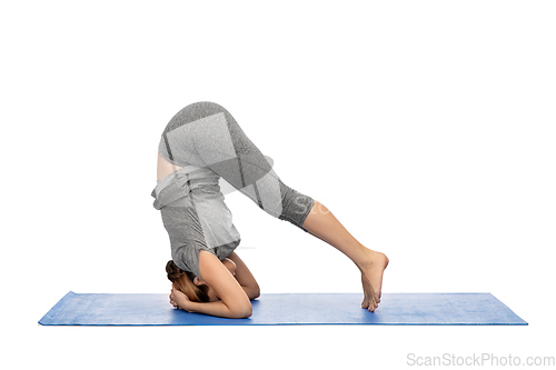 Image of woman making yoga in headstand pose on mat