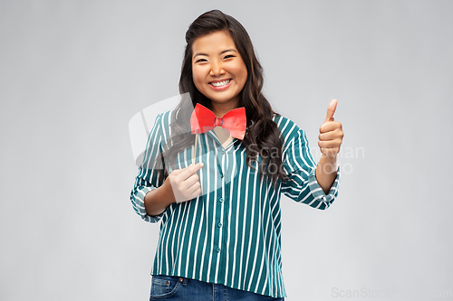 Image of happy asian woman with party bow showing thumbs up