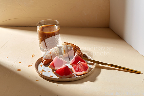 Image of glass of coffee, croissant and grapefruit on table