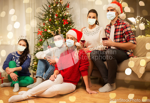 Image of friends in masks drinking wine on christmas