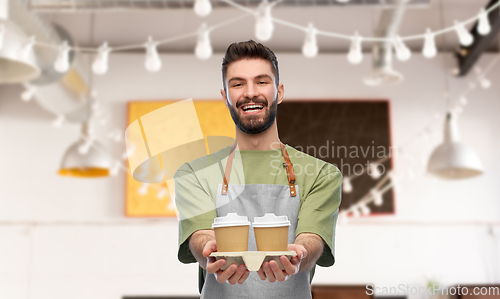 Image of happy smiling barman in apron with takeaway coffee