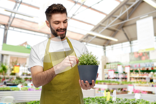 Image of smiling male gardener with flower in pot at shop